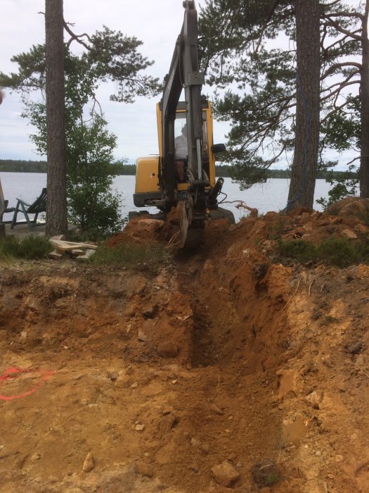 Grävmaskin som gräver mark vid en strand för att förbereda för tillbyggnad av sommarstuga.