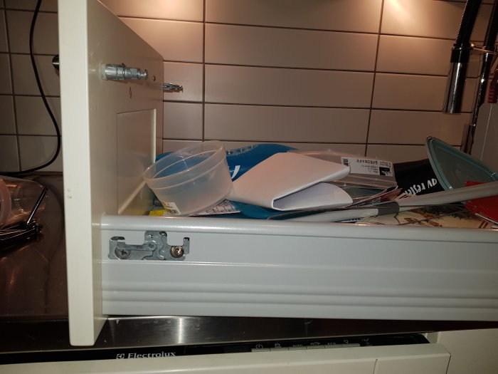 Kökslåda öppen med skruvar och beslag synliga, disklok och föremål ovanpå.