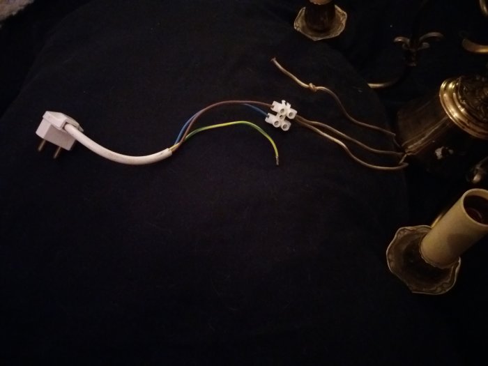 Elsladd med europeisk kontakt och avskalade kablar mot en mörk bakgrund med ljusstakar.