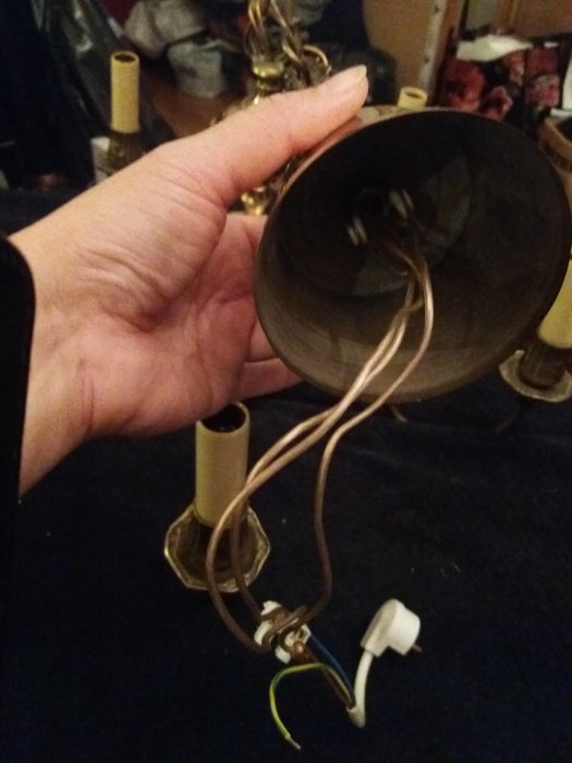 Hand som håller i en demonterad taklampa med synliga sladdar och ljuskällans hållare.