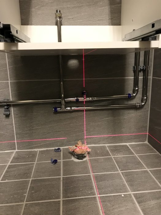 Installation av rör under handfat med lasernivellering, synliga vattenledningar och avlopp med kall- och varmvattenrör.