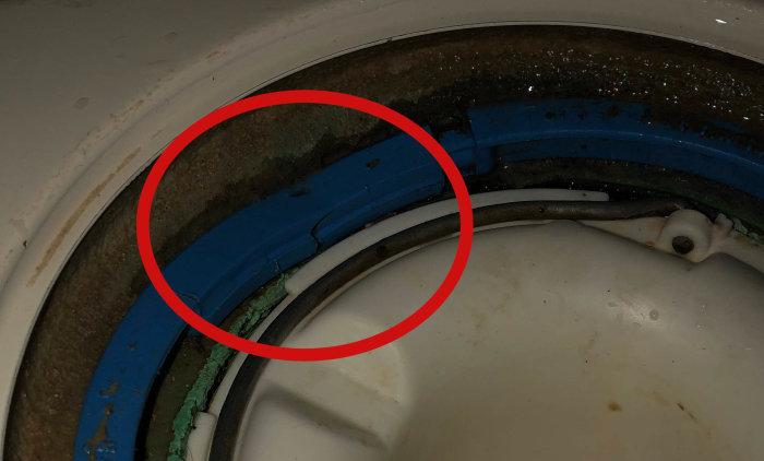 Sprucken klämring markerad med rött inuti en toalettstol, vilket indikerar en potentiell funktionsbrist.
