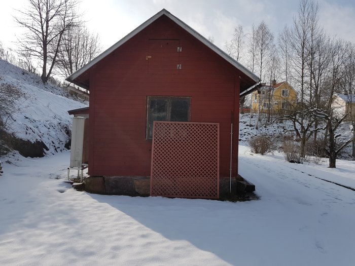 Ett rött gammalt garage på en snötäckt mark med stenfot och omgivande vinterlandskap.