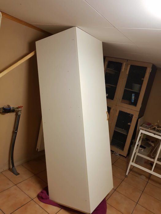 En vit garderob som står lutad i en källare klar för flytt.