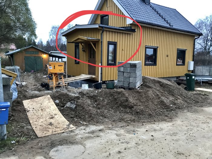 Nybyggt hus med markerat takområde som visar på felkonstruktion, omringat av byggmaterial och grushög.