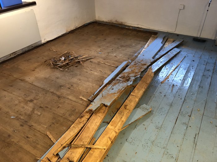Golv med upprivna trasiga träplankor och spillror i ett äldre hus som renoveras.