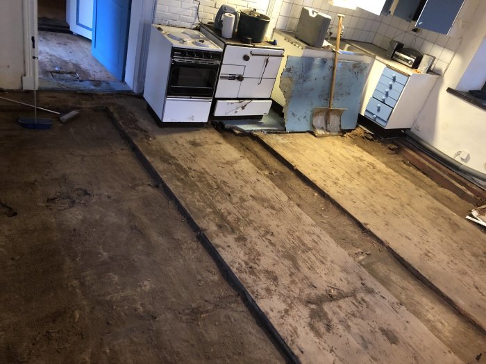 Kök med upprivet trägolv som avslöjar underliggande jord och mullbänk.