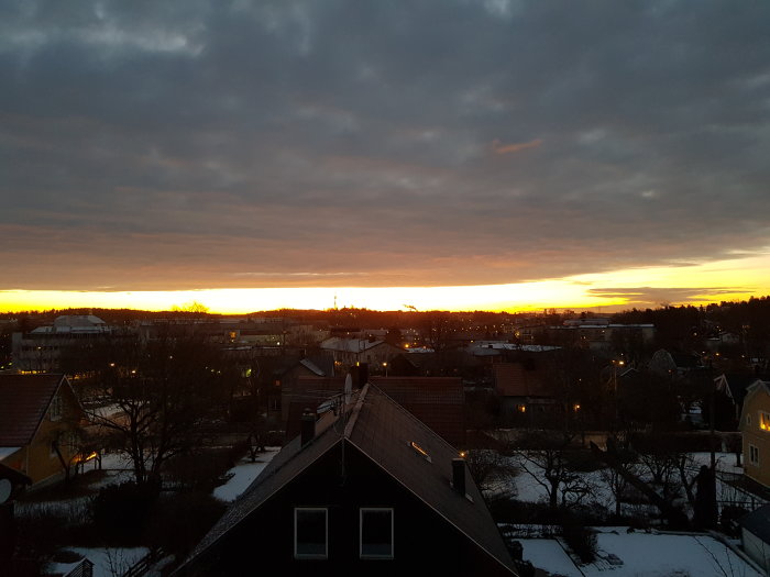 Soluppgång över en snötäckt stad med hus, träd och moln på himlen.