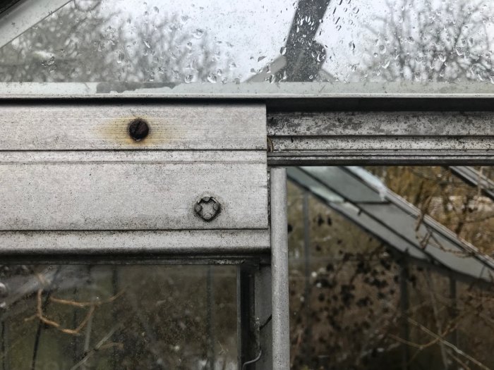Närbild på ett växthus med trasiga rutor och slitna aluminiumramar som behöver repareras.
