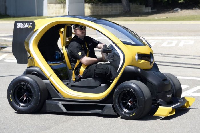 Man kör en gul och svart Renault Twizy moddifierad för sport, synlig på en asfalterad yta.