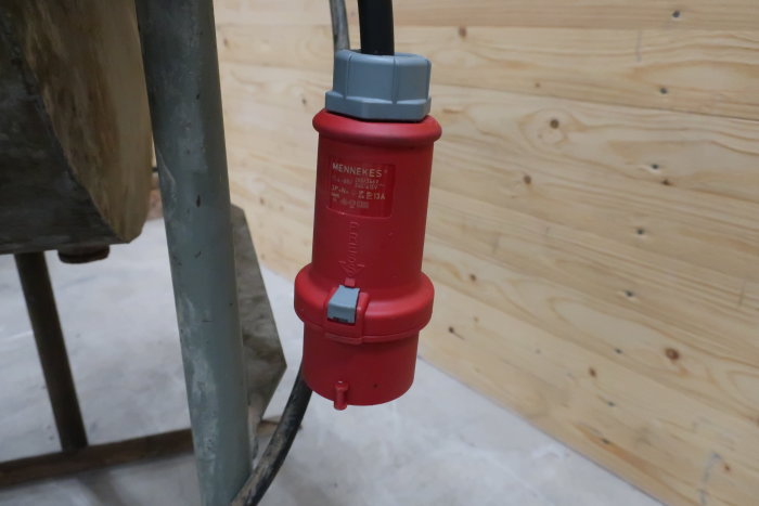 Röd 3-fas Mennekes stickpropp mot trävägg, märkt 220/380V för slipmaskin.