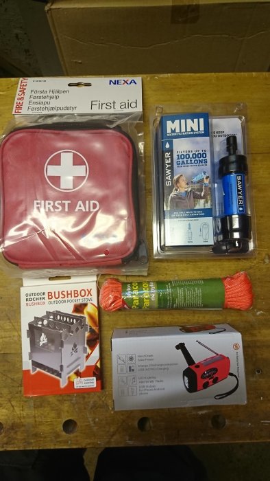 Första hjälpen-kit, vattenreningsfilter, tändstål, fickkök och handvevad solradio på arbetsbänk.