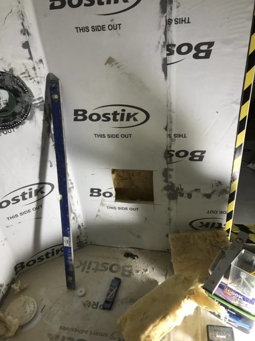 Renoveringsarbete på badrum med isoleringsmaterial, byggverktyg och vägg med Bostik-logotyp.