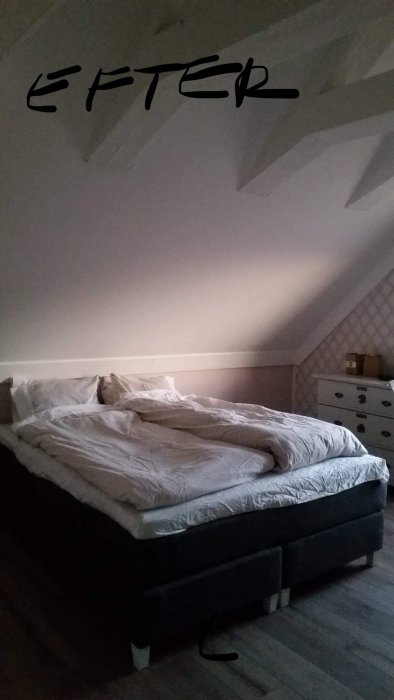 Sovrum efter renovering med säng, ljusa väggar och mörkt golv.