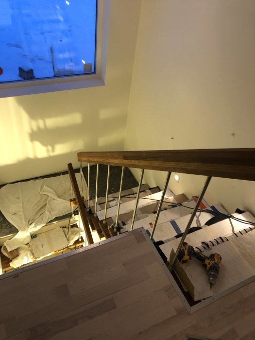 Trappa under renovering med trästeg, räcke och verktyg på en skyddad golv.