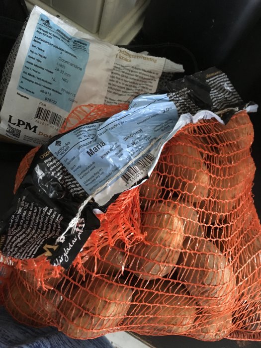 Nät med potatisutsäde "Gourmandine" och etikett för "Maria" i en svart låda.