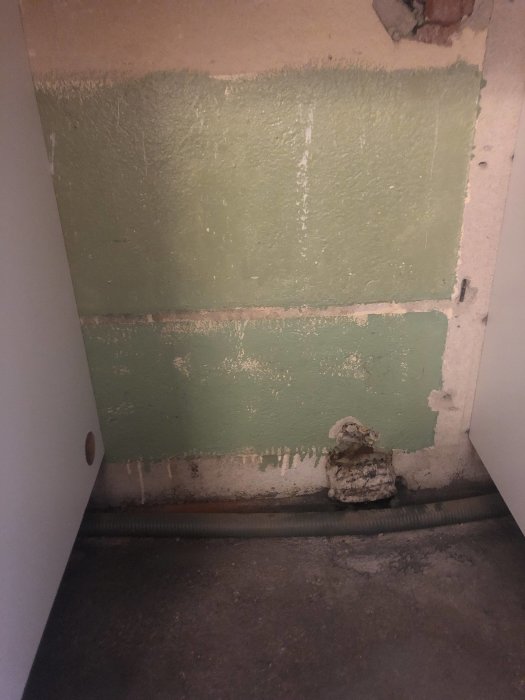 Väggutrymme för diskmaskin med synligt rör och gasslang på betonggolv.