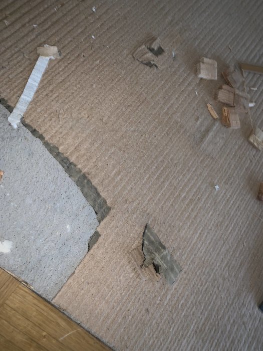 Delvis upprivet golv avslöjar lumppapp och möjligt svartlim under 60-talsgolvet.