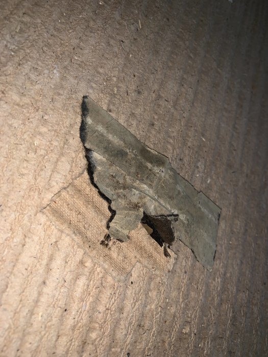 Delvis upprivet gammalt golv som visar lumppapp och ett svart skikt som kan vara svartlim.