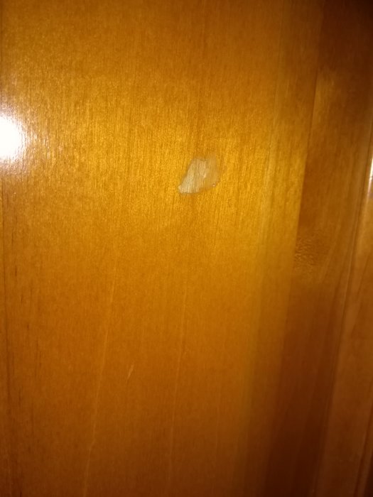 Skada på en träffärgad kökskåpslucka med en avflagad yta mitt på luckan.