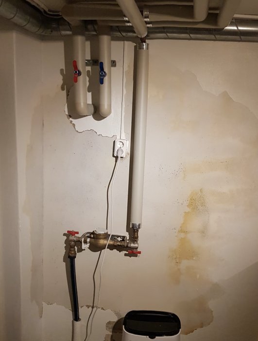 Vägg i tvättstuga med tecken på vattenläckage runt rörgenomföring och fuktfläckar.