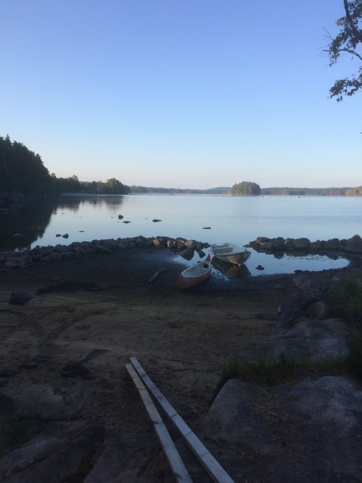 Vykortsvy över en sträcka med vikande vattenlinje längs strandkanten, båtar och träplank på marken.