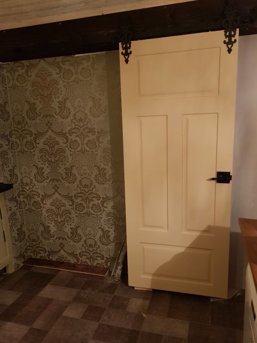 Ny målad dörr i rum med mönstrad tapet och schackrutigt golv.