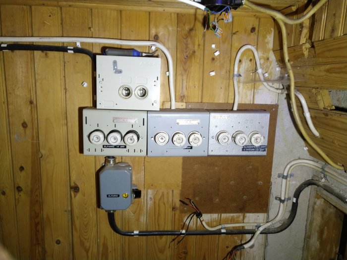 Elektrisk central före renovering med äldre mätare och oorganiserade kablar på en trävägg i källare.
