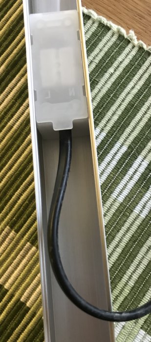 Kabel dragen genom ett hål i sidan av en belysningsarmatur på en randig matta.