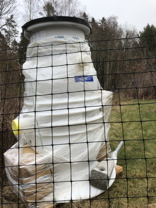 Förpackad avloppsreningsanordning står på en tomt, inplastad och redo för installation.