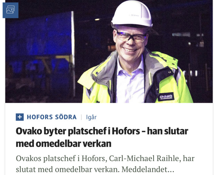 Leende man i skyddshjälm och reflexjacka på en industriplats om natten.