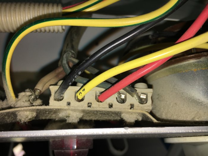 Dammsamling bakom omgjorda elektriska anslutningar med färgkodade kablar och säkringsblock.