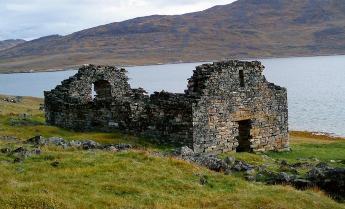 Ruin av stenhus från medeltiden vid en sjö, omgivet av berg och öppen terräng.