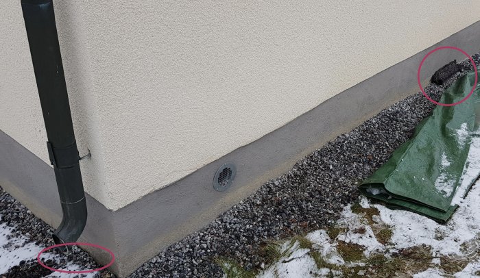 Stuprör anslutet till husvägg bredvid ventilation och dräneringsgrus, med markvattnet synligt och cirkelmarkerat.