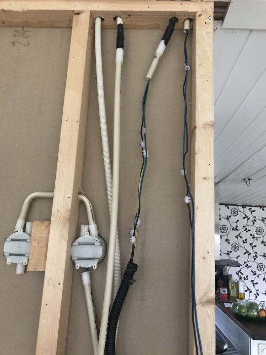 Rör och elektriska kablar som är amatörmässigt installerade i en öppen väggkonstruktion i ett kök.