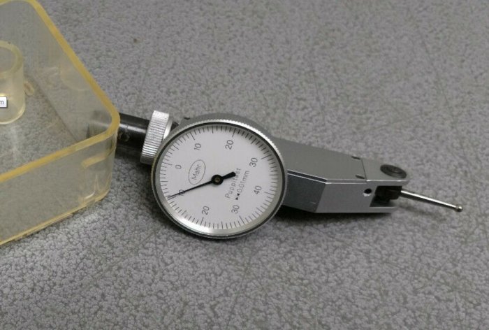 Begagnad tysk vippindikator med vridbar mätur och mätpinne på grått underlag.