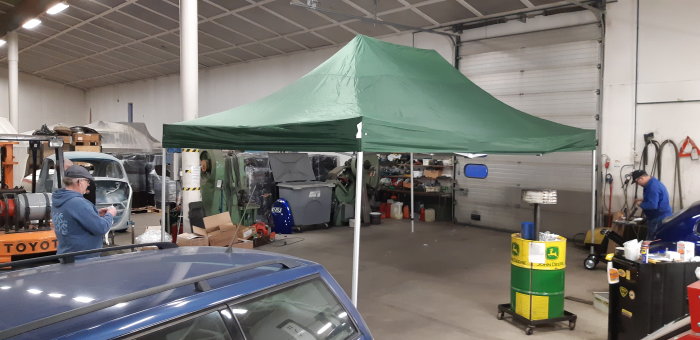 Stort grönt popup-tält i en verkstad med personer som arbetar och fordon runtomkring.