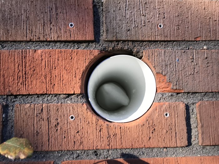 Plastventilationsrör monterat i röd tegelfasad, sett i närbild från ovansidan.