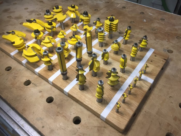 Samling av olika profilerade frässtålar på en organiserad träplatta i en verkstad.