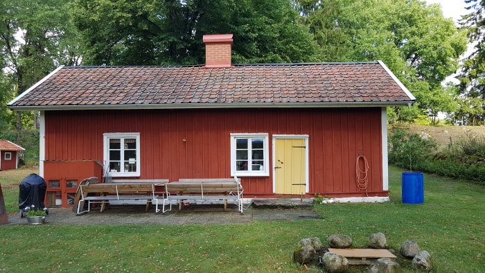 Rött trähus med gult dörr, uteplats och stenomgärdad tomt, landlig miljö.