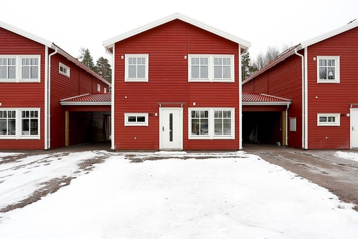 En nyproducerad röd radhuslänga med ett snötäckt framsidesområde redo för trädgårdsdesign.