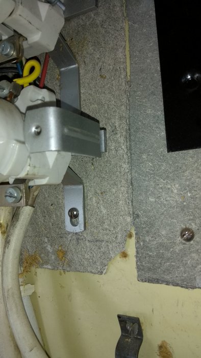 Gammal grå skiva bakom elcentral, möjlig asbesthaltig isolering.