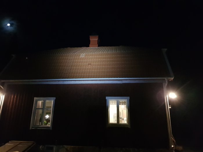 Ett hus i kvällsbelysning med nyinstallerad rökgenomföring i plast på taket och öppna fönster.