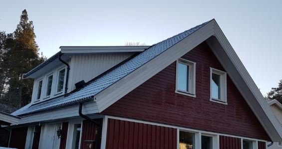 Nybyggda stora takkupor på ett rödmålat hus med vit knut och nytt grått tak, i skymningen.