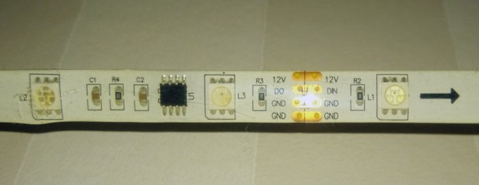 LED-list med tre lysande blå lampor, komponenter och märkningar för elektrisk anslutning.