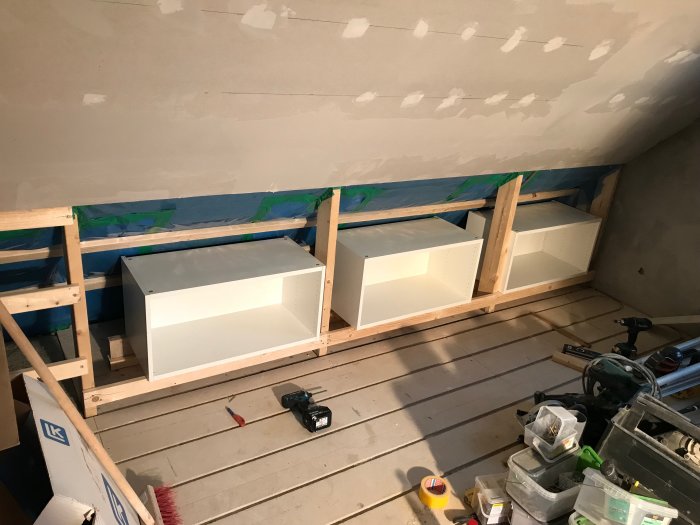 Inbyggnadsarbete med vita skåpsstommar på träställning och verktyg på golvet under renovering.