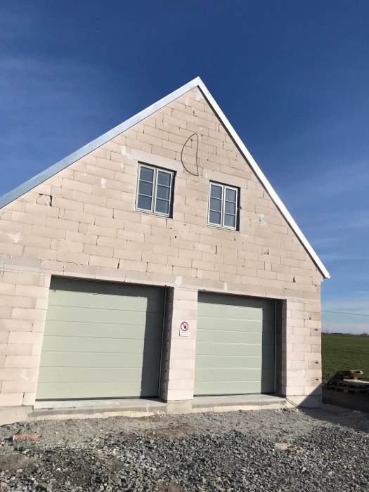 Nybyggd tvågaragebyggnad i ljus tegel med två gröna garageportar under en klarblå himmel.