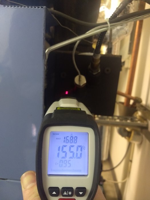 IR-termometer pekar på en RGT-givare med temperaturavläsning 159,0 °C på en värmepannans rökrör.