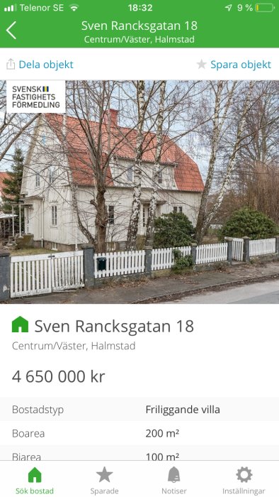 En vit villa med rött tak omgiven av träd och ett vitt staket med fastighetsmäklarens logotyp och information.