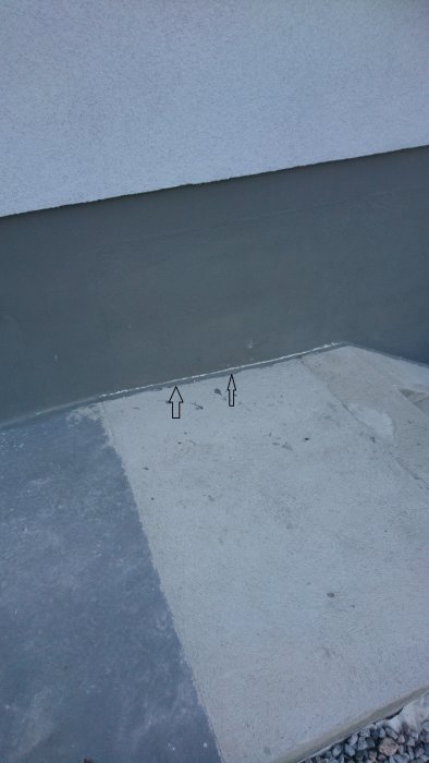 Spricka vid skarven mellan en betongtrappa och en vägg markerad med två pilar.